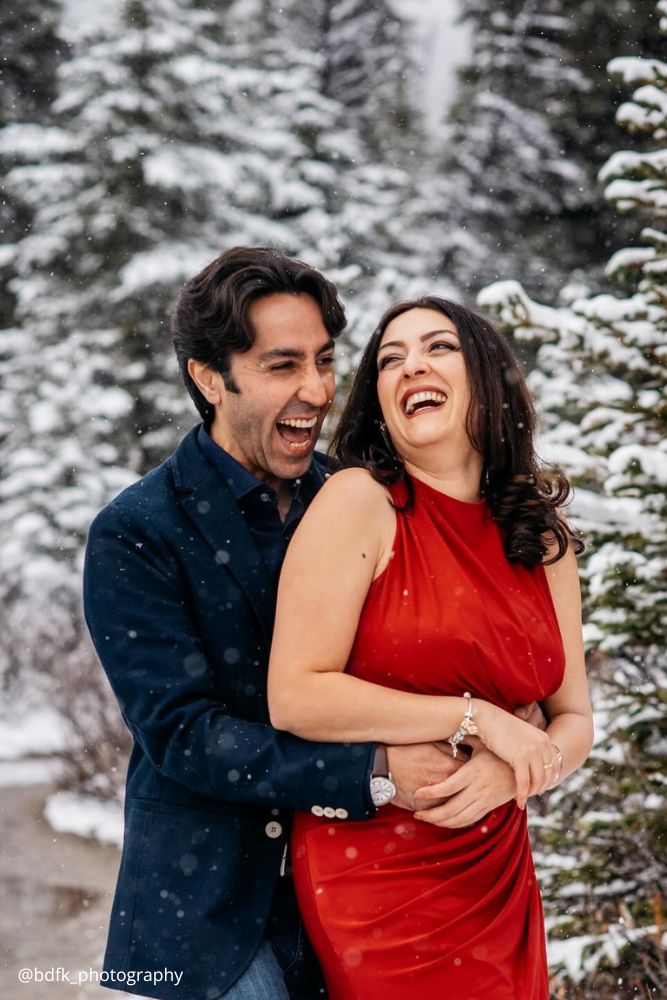 winter engagement photos happy love couple girl in red dress falling snowflakes bdfk photography