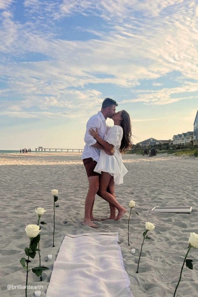 beach proposal ideas kissing couple at the beach decorated with white roses on the sand brilliantearth