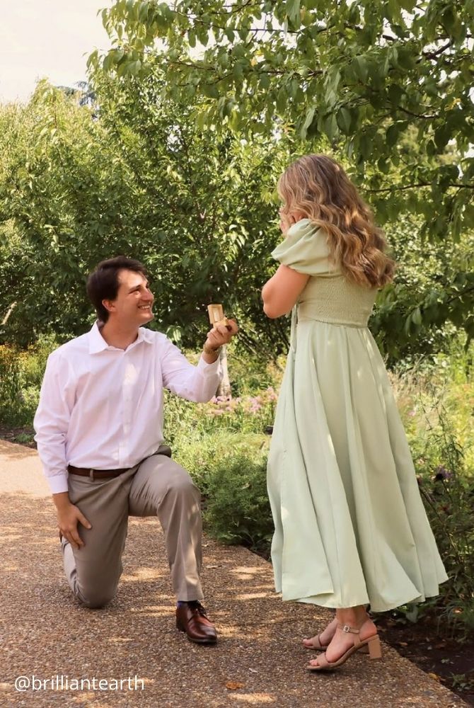 cheap proposal ideas man proposing on one knee to surprised woman in light green dress on sunny garden brilliantearth