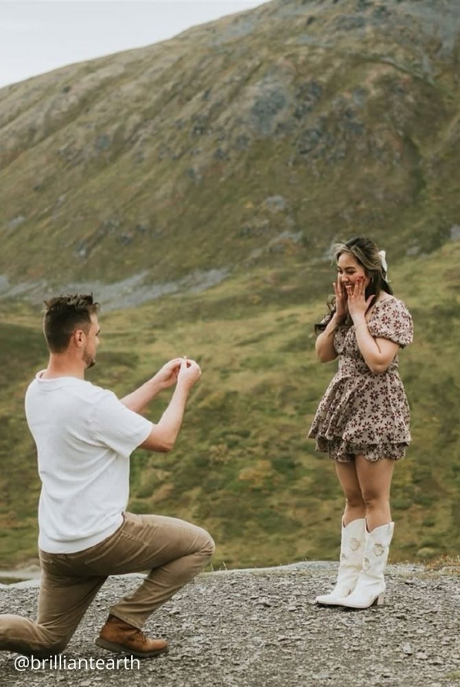 cheap proposal ideas man proposing to surprised woman against green mountain backdrop brilliantearth
