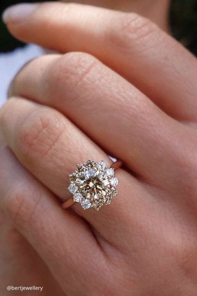 solitaire engagement rings ring on the finger in white gold with round stones and small flower shaped surrounding bertjewellery