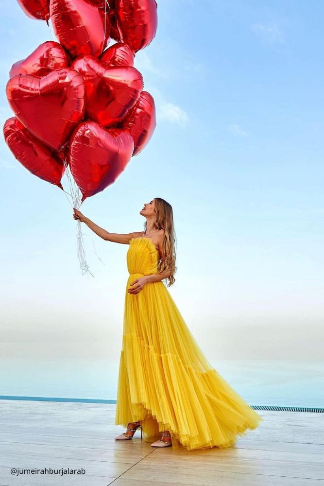 valentines day proposal girl on the seaside in yellow dress with lot of red heart shaped baloons in her hand jumeirahburjalarab